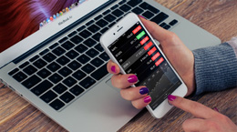 Person checking stocks on smartphone near laptop