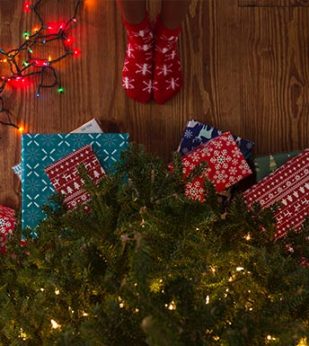 Wrapped gifts under a Christmas Tree with person wearing socks nearby