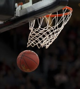 A basketball goes through a hoop on a darkened stadium.