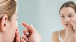 A woman puts in contact lenses in the mirror