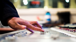 Up close of a hand turning up a levels on an audio mixing board