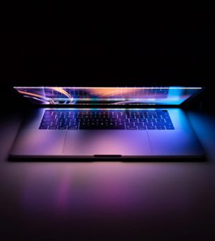 A laptop half closed with a colorful screen reflecting against a dark background