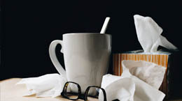 Mug of a hot beverage next to tissues and a pair of glasses