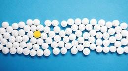 White tablet pills on a blue background with one differentiating yellow pill