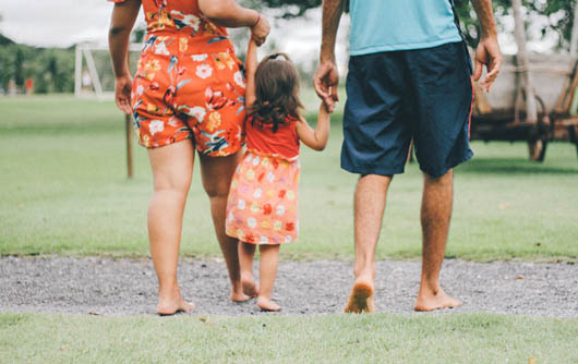 Two adults walk with a child between them holding hands.