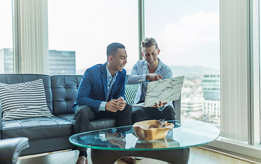 Two men smile while looking at something on a laptop