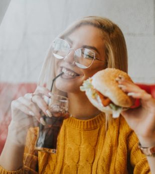 A woman smiles while holding a burger and soda