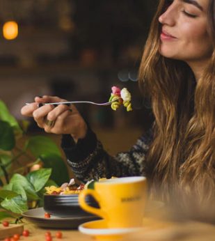 A woman sits at a table and brings a forkful of food to her mouth