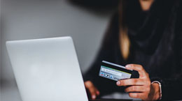 A person holds up a credit card while on a laptop